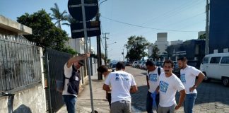 homens usando a mesma camiseta em volta de um bueiro aberto em uma calçada de rua de paralelepípedos