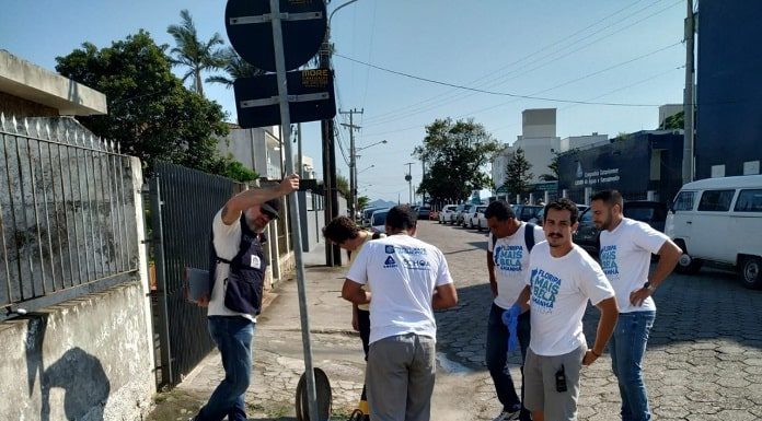 homens usando a mesma camiseta em volta de um bueiro aberto em uma calçada de rua de paralelepípedos