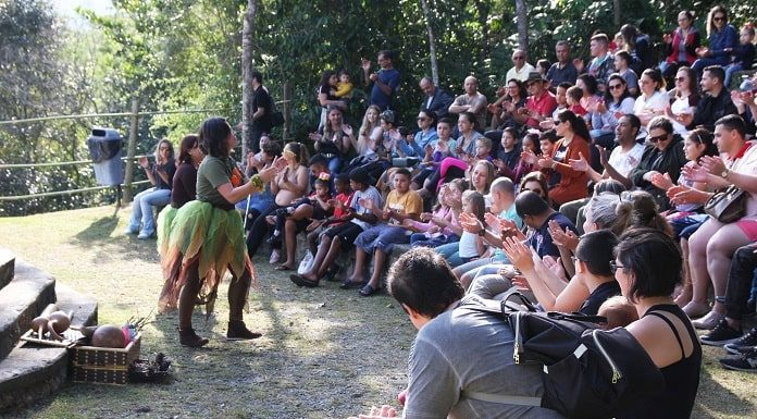 mulher fantasiada se apresenta para plateia cheia em pequeno anfiteatro ao ar livre