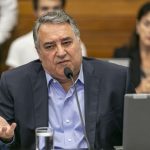 raimundo colombo gesticula falando em um micreofone, sentado em uma bancada com um computador à frente