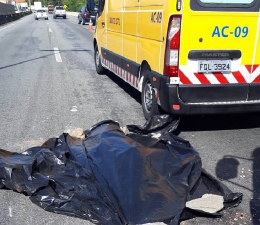 Em SJ, motoqueiro morre atropelado na BR 101 por caminhão e motorista foge corpo no chão coberto por lona preta com pedras prendendo e ambulância da als ao lado