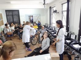 em uma sala, algumas pessoas em cadeiras de rodas, outras em carterias e outras com jaleco em pé
