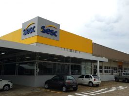 fachada externa da unidade do sesc com placa e carros estacionados na frente