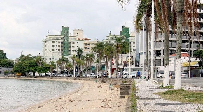 a orla da praia, sem ninguém, com calçada com coqueiros e prédios ao fundo