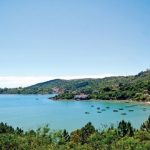 vista superior da praia calma com alguns barcos na água e morros com muita vegetação em volta