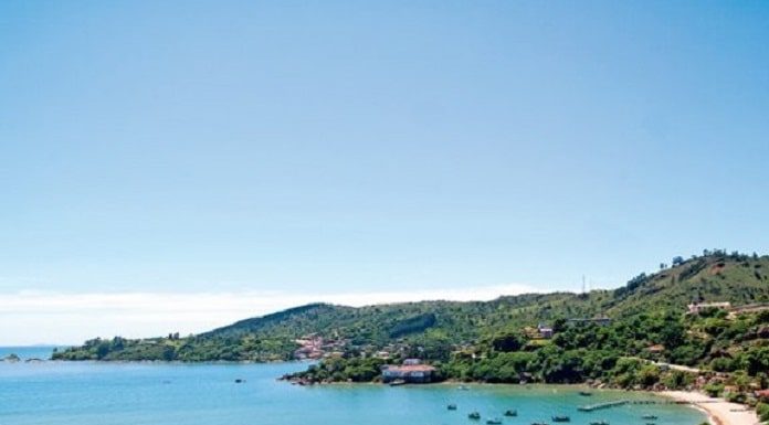 vista superior da praia calma com alguns barcos na água e morros com muita vegetação em volta