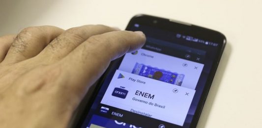 Divulgados os locais de prova do Enem, que ocorre em 3 e 10 de novembro mão sobre um smartphone com logo do enem na tela