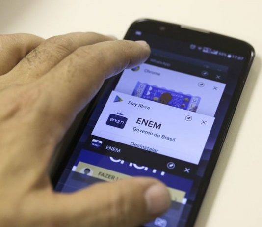 mão sobre um smartphone com logo do enem na tela