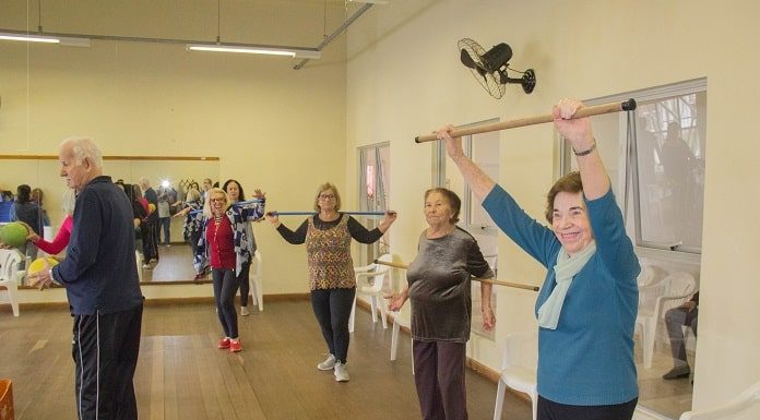 idosas se exercitando em pé em grande salão com espelhos