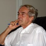 belmiro visto de lado com a mão no rosto segurando uma caneta e contemplativo