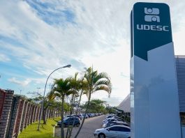 torre com inscrição da udesc no topo ao lado de prédio e estacionamento do campus