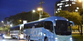 dois ônibus passando por rua arborizada caracterizados com o logo 4bus