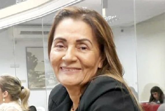 bernadete olha sorridente para a foto sentada em uma mesa
