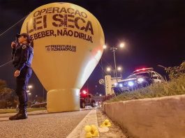 balão inflável da operação lei seca em via pública com uma agente da guarda ao lado e viatura na cabeceira da ponte