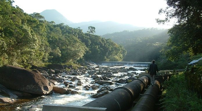 canos de adutora ao lado do rio cubatão em meio à vegetação