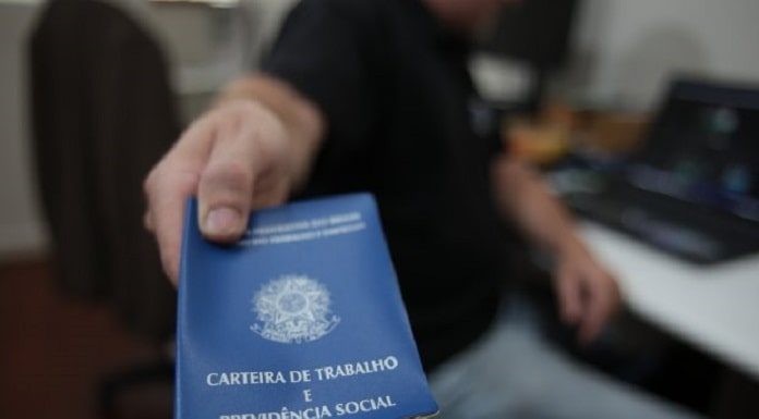 homem aponta para a câmera uma carteira de trabalho e previdência social