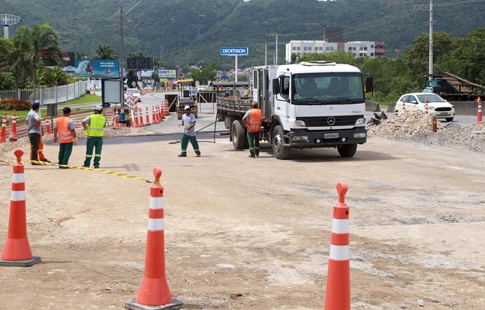 obra reconstrucao galeria pluviar sc-401 desvio-min caminhões e operários sobre a pista onde há cones e montes de areia