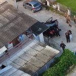 foto aérea de casa com telhado de zinco com diversos policiais na frente da casa na rua