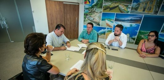 Prefeitura vai doar suplementação alimentar às gestantes em Palhoça na ponta de uma mesa o prefeito camilo martins assina documento com outros homens e mulheres sentados em volta olhando
