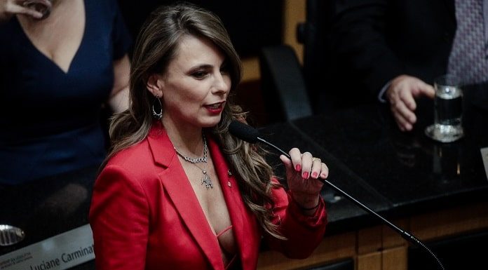 deputada paulinha discursando ao microfone com a roupa decotada na cerimômia de posse