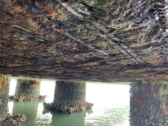 estrutura de pilares de concreto sobre a água, sendo que a parte superior está desgastada com ferros à mostra