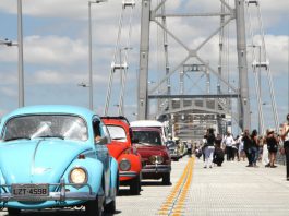 fuscas e outros carros antigos passando sobre a ponte Hercílio Luz com pessoas em volta