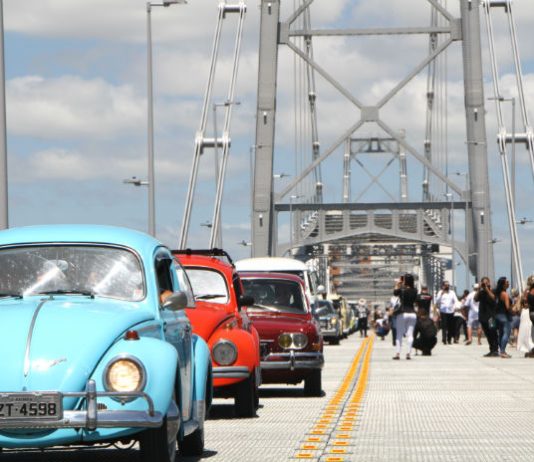 fuscas e outros carros antigos passando sobre a ponte Hercílio Luz com pessoas em volta
