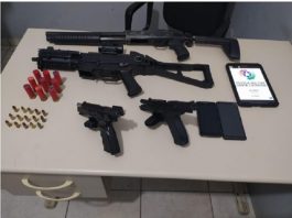 PM apreende armas de alto calibre na Praia do Pontal, em Palhoça armas dispostas sobre uma mesa com as munições, celulares e um tablet com logo da pm ao lado