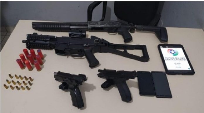 armas dispostas sobre uma mesa com as munições, celulares e um tablet com logo da pm ao lado