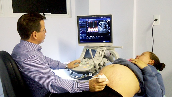 médico faz ultrassonografia em mulher com grande barriga deitada e os dois olham para o monitor