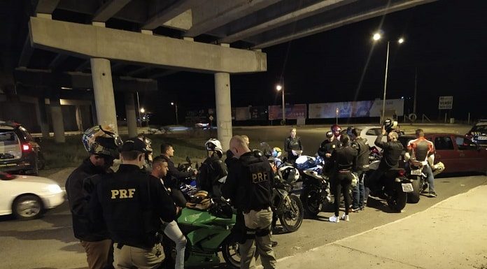 agentes da prf ao lado de diversas motos com pessoas em volta de noite