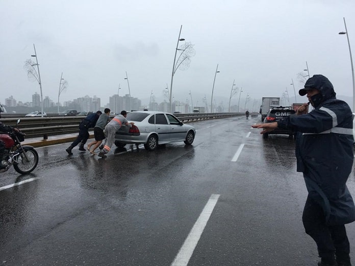 veículo vectra sendo empurrrado por três homens em cima da ponte, com guarda ao lado em dia de chuva