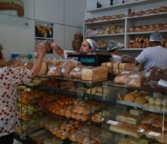 padaria com atendente passando produto para cliente por cima do balcão cheio de pacotes de pão