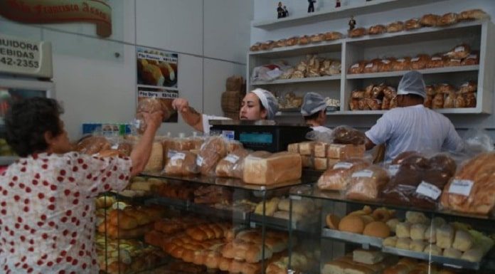 padaria com atendente passando produto para cliente por cima do balcão cheio de pacotes de pão