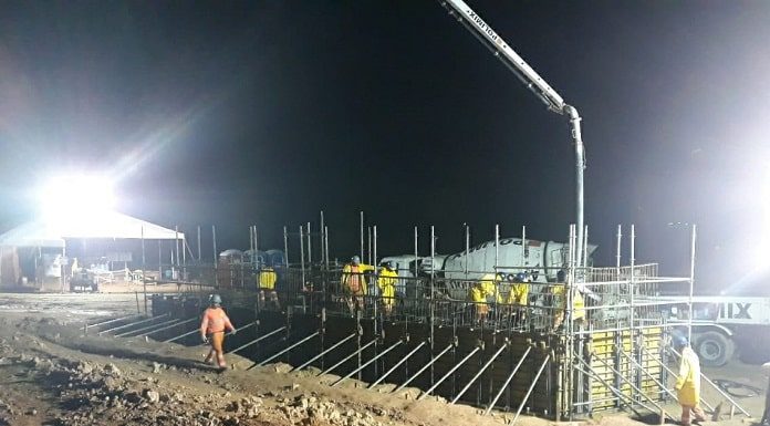 dois trabalhadores em volta de grande estrutura de armada de madeira e ferro para colocação de concreto em área de terra