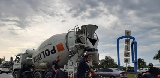 Betoneira derruba concreto na pista e complica entrada para ilha dois agentes da guarda limpam concreto caído atrás da betoneira e carros passando em volta