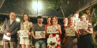 nove pessoas, entre homens e mulheres, em um palco, sorridentes e mostrando certificado nas mãos