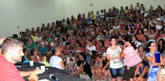 auditório lotado, a maioria mulheres, com algumas pessoas sentadas em palco à frente em uma mesa