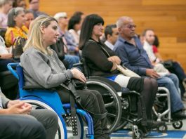 mulheres e homens em cadeiras de roda à frente das poltronas de um auditório com outras pessoas sentadas