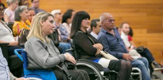 mulheres e homens em cadeiras de roda à frente das poltronas de um auditório com outras pessoas sentadas