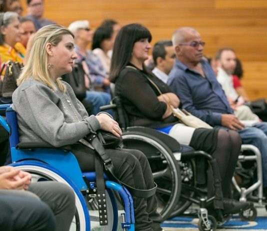 SC criou 8 mil empregos para pessoas com deficiência em quatro anos mulheres e homens em cadeiras de roda à frente das poltronas de um auditório com outras pessoas sentadas