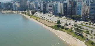 foto aérea da beira-mar mostrando o mar, pequena praia, avenida e fileira de prédios ao lado