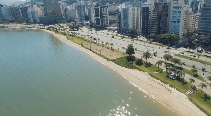 foto aérea da beira-mar mostrando o mar, pequena praia, avenida e fileira de prédios ao lado