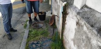 líquido azul escorrendo pela calçada a partir de cano no muro e um bueiro aberto ao lado, com dois fiscais em volta