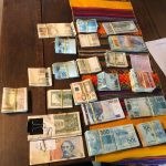 mesa com maços de dinheiro de diversas moedas de países diferentes, presas com elásticos
