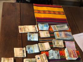 mesa com maços de dinheiro de diversas moedas de países diferentes, presas com elásticos