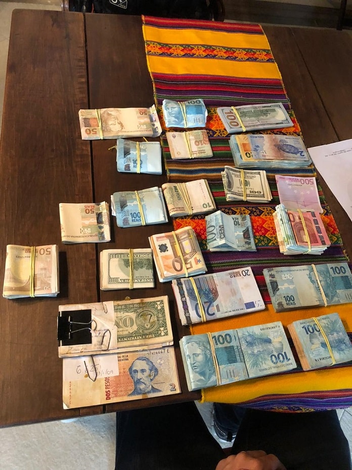mesa com maços de dinheiro de diversas moedas de países diferentes, presas com elásticos