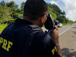 agente da prf mira radar em veículos passando em rodovia de pistas simples e plana no meio da mata