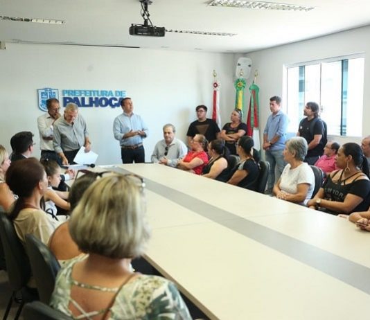 grande mesa com pessoas sentadas e em pé em volta e prefeito em pé na ponta