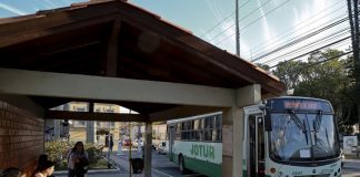 ônibus da jotur parado em frente a um ponto de ônibus de tijolos a vista em uma praça